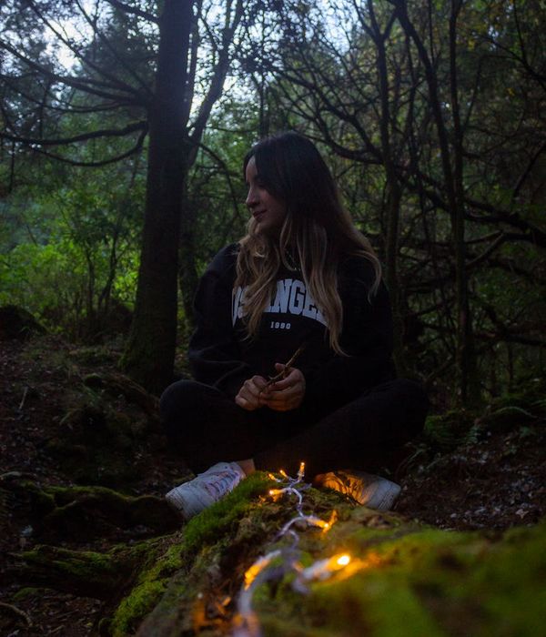 Woman meditating peacefully with glowing amber light in a mossy green forest.